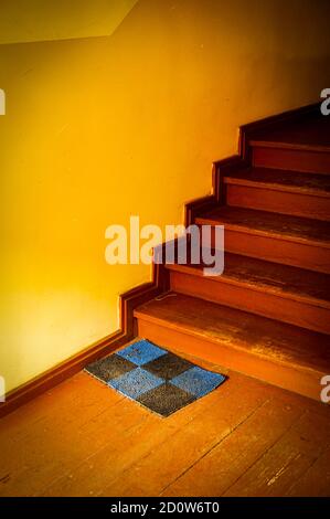 Vertikale Aufnahme einer alten hölzernen Treppe und einer Matte Bei einem Saal in braun gemalt Stockfoto