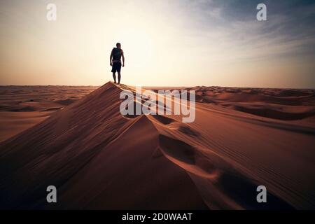 Wüstenabenteuer. Junger Mann, der auf Sanddüne gegen Sonnenuntergang läuft. Abu Dhabi, Vereinigte Arabische Emirate Stockfoto