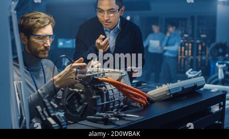 Zwei professionelle Kfz-Ingenieure mit einem Tablet-Computer und Inspektion Werkzeuge führen ein Gespräch beim Testen eines Elektromotors In A High Stockfoto