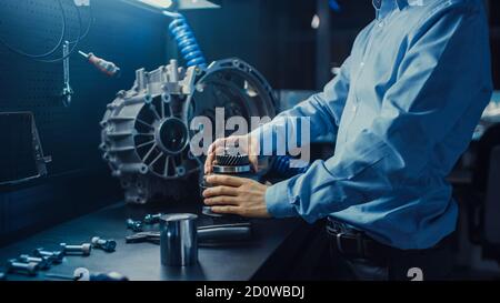 Der professionelle Automobilingenieur in Brillen arbeitet an Getriebezahnrädern in einem innovativen High-Tech-Labor mit Computerbildschirmen. Stockfoto