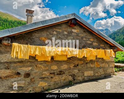 Berghütte aus Stein mit gelben Kleidern, die draußen vor den trockenen Alpen hängen, Trentino, Italien, Europa Stockfoto