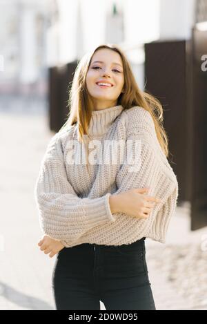 Eine junge Frau in einem beigefarbenen Strickpullover geht herum Die Stadt und lächelt wunderschön Stockfoto