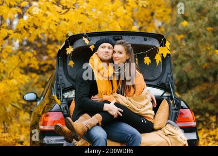 Ein glückliches Paar sitzt auf dem Kofferraum eines Autos und genießt den Blick auf den Herbst. Das Konzept der Reise-und Wochenendferien. Stockfoto