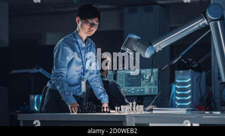 Professioneller japanischer Entwicklungsingenieur testet eine künstliche Intelligenz-Schnittstelle, indem er Schach mit einem futuristischen Roboterarm spielt. Sie sind in Stockfoto