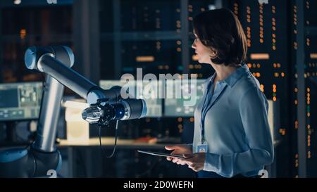 Ingenieurin mit Tablet Computer Analysieren Sie, wie ein futuristischer Roboterarm funktioniert und ein Metallobjekt bewegt. High-Tech-Forschungslabor mit modernen Stockfoto