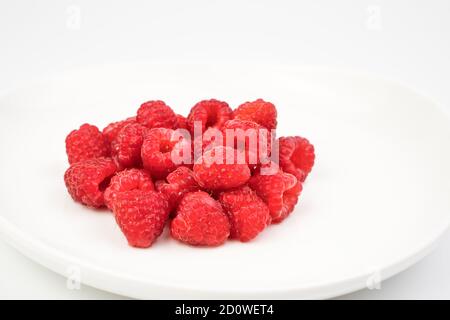 Frische Himbeeren in kleinen Mengen werden auf einem weißen Teller auf einem hellen Hintergrund platziert. Stockfoto