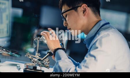 Professioneller japanischer Elektronikentwickler in blauem Hemd ist Löten Eine Leiterplatte in einem High-Tech-Forschungslabor mit Modern Stockfoto