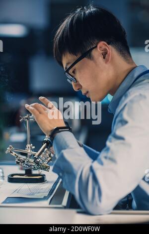 Vertikale Aufnahme eines professionellen japanischen Elektronikingenieurs in Blue Shirt löt eine Leiterplatte in einem High Technische Forschung Stockfoto