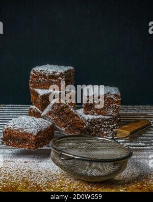 Vertikale Aufnahme von köstlichen Brownies mit Puderzucker bedeckt, neben einem Siefter Stockfoto
