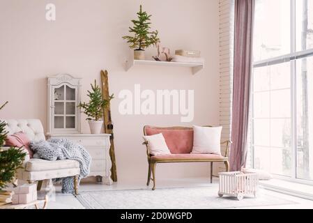 Ein rosa Vintage-Sofa mit Kissen steht neben dem Fenster im Wohnzimmer oder Kinderzimmer, dekoriert für Weihnachten oder Neujahr, im Haus. Mini Stockfoto