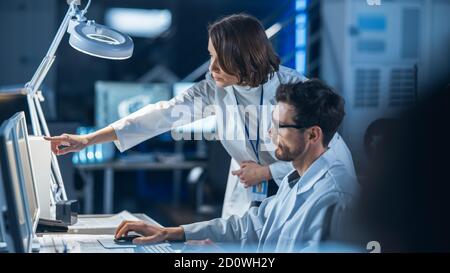 Entwicklungsingenieur für Maschinenmotoren, der an seinem Schreibtisch am Computer arbeitet, spricht mit dem Projektmanager und zeigt Prototyp-Komponente. Team von Fachleuten Stockfoto