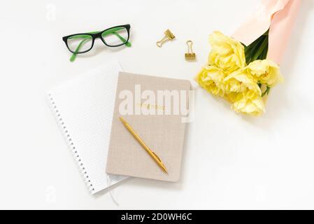 Trending minimalistischen flachen Lay eines Bloggers Arbeitsplatz. Notizblock, Stift, goldfarbene Büroklammern und ein Bündel gelber Tulpen, Brille, Tastatur auf einem W Stockfoto