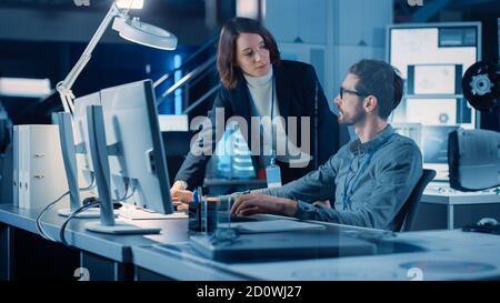 Futuristische Maschinenbauingenieurin, die am Computer an seinem Schreibtisch arbeitet, spricht mit weiblicher Projektmanagerin. Team von Fachleuten, die in arbeiten Stockfoto