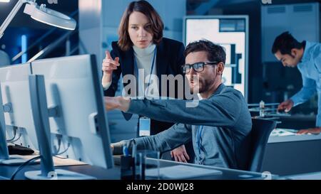 Futuristische Maschinenbauingenieurin, die am Computer an seinem Schreibtisch arbeitet, spricht mit weiblicher Projektmanagerin. Team von Fachleuten, die in arbeiten Stockfoto