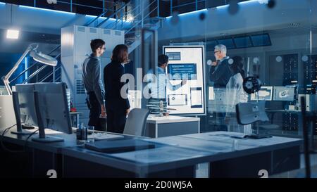 Ingenieure treffen in Technology Research Laboratory: Ingenieure, Wissenschaftler und Entwickler versammelten sich um beleuchteten Konferenztisch, reden und Stockfoto
