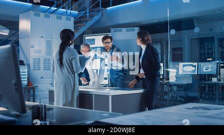 Ingenieure treffen sich im Roboterforschungslabor: Ingenieure, Wissenschaftler und Entwickler versammelten sich um beleuchteten Konferenztisch, sprechen, verwenden Stockfoto