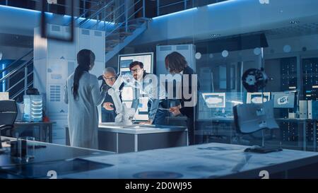 Ingenieure treffen sich im Roboterforschungslabor: Ingenieure, Wissenschaftler und Entwickler versammelten sich um beleuchteten Konferenztisch, sprechen, verwenden Stockfoto