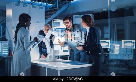 Ingenieure treffen sich im Roboterforschungslabor: Ingenieure, Wissenschaftler und Entwickler versammelten sich um beleuchteten Konferenztisch, sprechen, verwenden Stockfoto