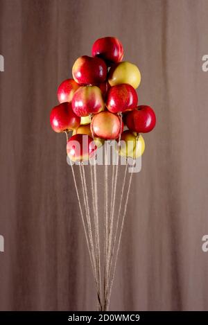 Ein Bündel von roten und gelben Äpfeln an einem Basteljutenseil, das wie Luftballons fliegt. Eine Erinnerung aus der Kindheit. Konzeptionelle Idee Stockfoto