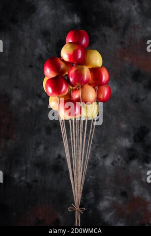 Ein Bündel von roten und gelben Äpfeln an einem Basteljutenseil, das wie Luftballons fliegt. Eine Erinnerung aus der Kindheit. Konzeptionelle Idee Stockfoto