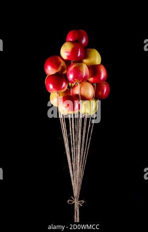 Ein Bündel von roten und gelben Äpfeln an einem Basteljutenseil, das wie Luftballons fliegt. Eine Erinnerung aus der Kindheit. Konzeptionelle Idee Stockfoto