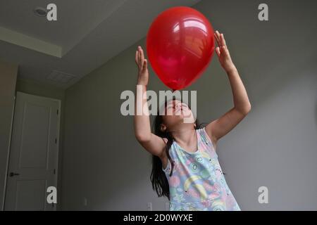 Fünf Jahre altes Mädchen spielt mit einem roten Ballon in Ein leerer Raum Stockfoto