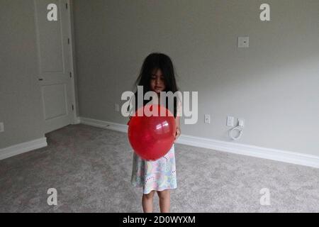 Fünf Jahre altes Mädchen spielt mit einem roten Ballon in Ein leerer Raum Stockfoto