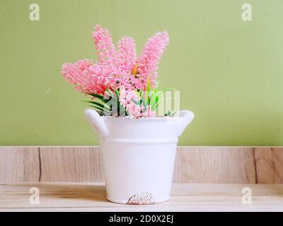Weißer Blumentopf aus Keramik mit rosa Kunstblumen auf Holzregal Stockfoto