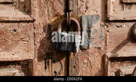 Das Schloss an der alten Holztür schloss sich. Rost auf dem Metallschloss. Die braune Farbe blättert an der alten Tür ab. Uralte Textur. Stockfoto