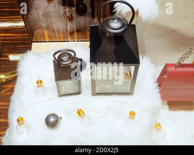 Große und kleine dekorative Laterne und andere Weihnachtsdekor auf Eine weiße Pelzmatte hinter dem Glas des Ladens Stockfoto