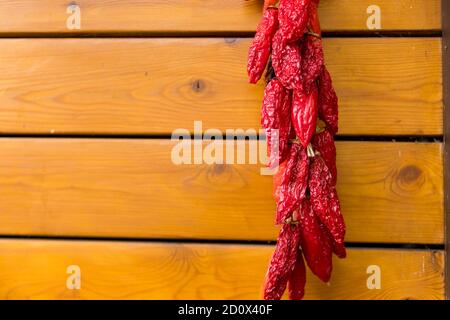 Rote Chilischoten auf dem Hintergrund der alten Holzwand.Schnur von frischen Bio-Paprika hängt draußen und trocken in der Sonne. Getrockneter Pfeffer Stockfoto