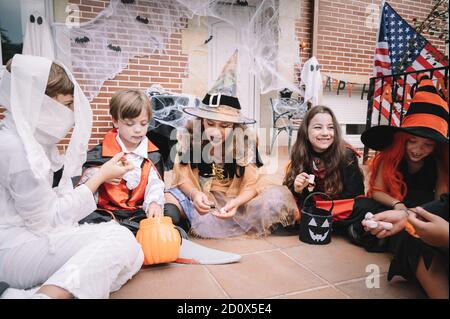 Kinder teilen und vergleichen ihre Süßigkeiten an Halloween sitzen auf Eine Etage Stockfoto