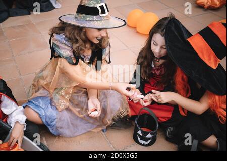 Kinder, die auf dem Boden sitzen und ihre Süßigkeiten vergleichen Halloween Stockfoto