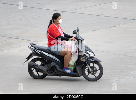 SAMUT PRAKAN, THAILAND, JULI 25 2020, EINE Frau in einer Schürze trägt Zutaten auf einem Motorrad. Stockfoto