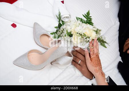 Ein Bräutigam hält die Hand der Braut. Die Hand der Braut ist mit Henna-Tattoos verziert. Im Hintergrund ein Blumenstrauß Stockfoto