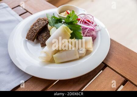 Fett, Schmalz. Snack für Wodka. Auf einem weißen Teller ist eine Zusammensetzung aus Gurken, rote Zwiebeln, gebratenes Brot und Knoblauch.Delicious Schweinefleisch Fett in Scheiben mit Zwiebeln und Stockfoto