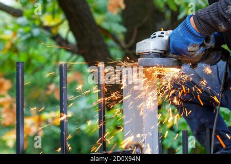 Unter der Schutzabdeckung des Winkelschleifers fliegen beim Schneiden von Metall helle, heiße Funken hervor. Stockfoto