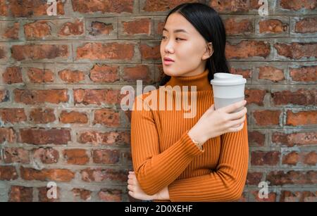 Portrait von jungen asiatischen Frau mit einer Tasse Kaffee gegen die Mauer. Urban Konzept. Stockfoto