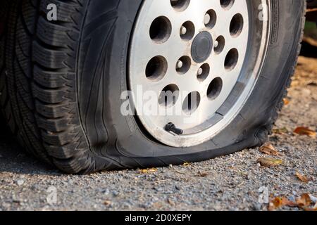 Ein Auto mit einem Platten Reifen ist auf einer unbefestigten Straße geparkt zu sehen. Stockfoto