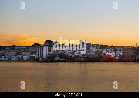 St. John's, Neufundland, Kanada der Himmel wird orange, wenn die Sonne hinter der Innenstadt von St. John's mit dem Ozean im Vordergrund untergeht. Stockfoto