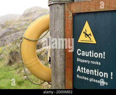 Ein zweisprachiges Parks Canada (Parcs Canada) Schild Warnung vor rutschigen Felsen, roches glissante in Französisch, und Rettungsring am Fort Rodd Hill und Stockfoto