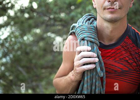 Ein männlicher Kletterer von kaukasischem Aussehen mit einem gewickelten Seil auf seiner Schulter. Hand in weißer Magnesia. Red Sports Trikot, Extremsport, Klettern. S Stockfoto