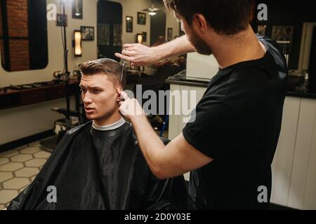 Friseur Falten Ohr, so dass ein Haarschnitt für einen jungen Mann in einem Friseurladen Stockfoto