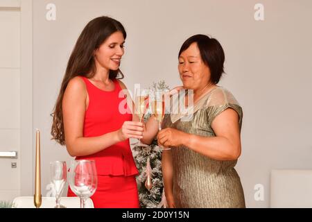 Blick auf zwei Frauen mit einem Toast mit Sektgläsern in der Nähe eines weihnachtlich dekorierten Tisch auf einem unscharf Hintergrund. Weihnachtsfeier Konzept. Stockfoto