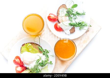 Pochierte Eier royale (benedict) auf Vollkornbrot, frischer Orangen- und Karottensaft, Avocado, Tomaten, grüner Salat Microgreens. Eine gesunde, leckere br Stockfoto