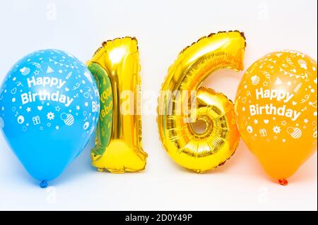 Aufblasbare Zahl 16 funkelnde metallische goldene Farbe mit blauen und gelben Ballons auf weißem Hintergrund isoliert. Nahaufnahme. Speicherplatz kopieren. Stockfoto