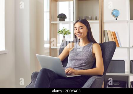 Lächelnde junge Geschäftsfrau, die in einem bequemen Sessel mit Laptop sitzt Gemütliches Büro Stockfoto