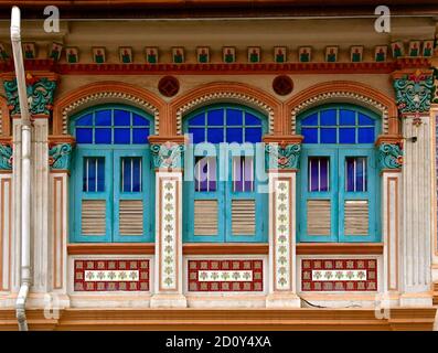 Restauriertes chinesisches peranakan-Ladenhaus mit blauen Lamellenfenstern aus Holz und verzierten Bögen, Architraven und floralen Mosaikfliesen. Stockfoto