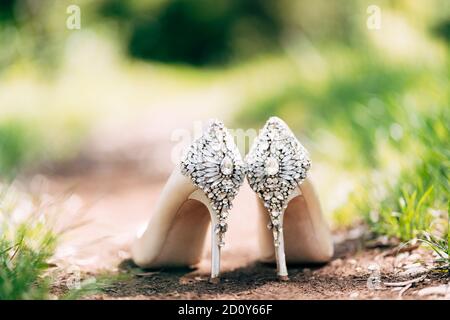 Schuhe der Braut mit einem Hintergrund mit Steinen auf dem Boden in der Natur mit geringer Tiefe des Feldes verziert. Stockfoto