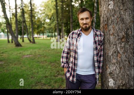 Bärtiger Mann, der in der Nähe des Baumes im Sommerpark steht Stockfoto